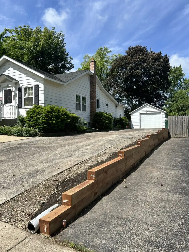 Newly installed timber retaining wall along a residential driveway providing structural support, erosion control, and a clean landscape border by BlackRock Outdoor Living.